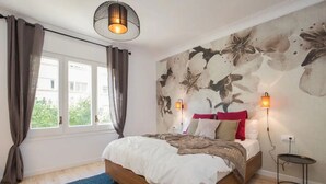 Une chambre à coucher avec un lit, des rideaux, une fresque murale et une petite table avec une lampe.