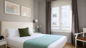 Ein Hotelzimmer mit einem Bett, einem Nachttisch, einer Lampe, einem Sessel und einem Fenster mit Vorhängen.