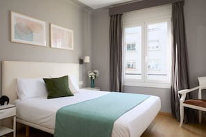 A hotel room with a bed, a nightstand, a lamp, a chair, and a window with curtains. - Casa Cosi - Casanova 5 (Barcelona)