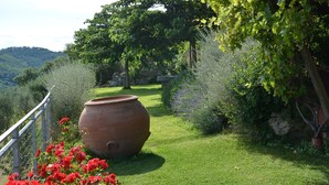 A garden with a large terracotta pot, a metal fence, and red flowers. - LA RONDINAIA. CHARMING HOUSE WITH GARDEN AND POOL. AMAZING VIEW (CASTELNUOVO BERARDENGA)