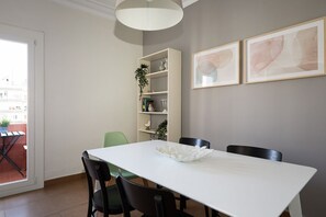 A dining area with a white table, black chairs, a white bookshelf, and two framed artworks on the wall. - Casa Cosi - Casanova 7 (Barcelona)