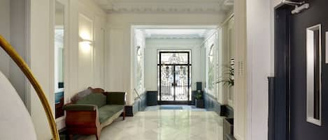 A hallway with a staircase, a green sofa, and a door with a decorative glass panel.