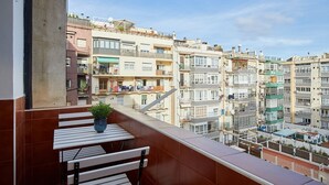 A balcony with a table and chair, overlooking a densely packed urban area with multi-story buildings. - Casa Cosi - Casanova 7 (Barcelona)
