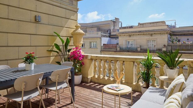 A terrace with a table and chairs, potted plants, and a view of surrounding buildings. - Casa Cosi - Terrace 1 (Barcelona)