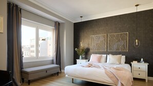 A bedroom with a large bed, a bench, a bedside table, and a window with curtains. - Casa Cosi - Terrace 1 (Barcelona)