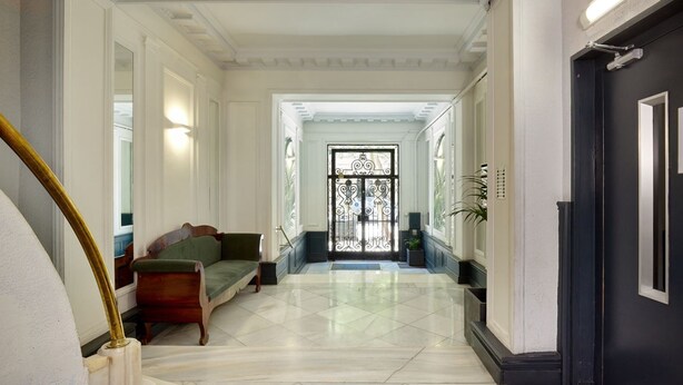 A hallway with a staircase, a green sofa, and a door with a decorative glass panel. - Casa Cosi - Terrace 2 (Barcelona)