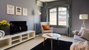 A modern living room with a flat-screen TV, a round coffee table, and a comfortable armchair. - Casa Cosi - Terrace 2 (Barcelona)