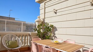 A patio with a wooden table and pink chairs, a white wicker chair, and a potted plant. - Casa Cosi - Terrace 2 (Barcelona)