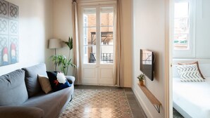 Un salon confortable avec un canapé, un téléviseur, une porte donnant sur un balcon et un sol à motifs.