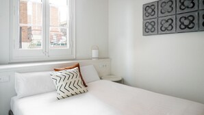 Une chambre à coucher comprenant un lit, une fenêtre, une table de chevet et un luminaire fixé au mur.