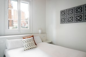 Ein Schlafzimmer mit einem Bett, einem Fenster, einem Nachttisch und einer Wandleuchte.