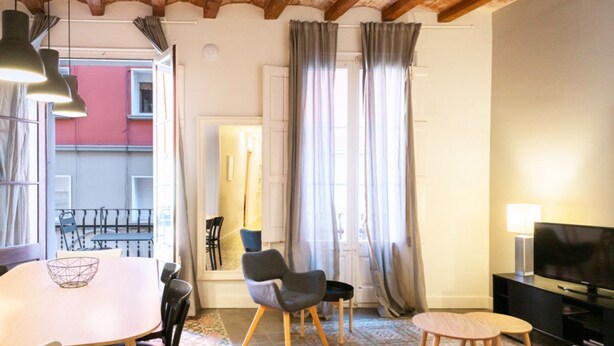 Ein gemütliches Wohnzimmer mit Essbereich, Fernseher und großem Fenster mit Vorhängen.