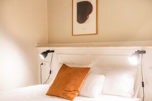 A neatly made bed with white linens and a single brown pillow, two bedside lamps, and a framed abstract artwork on the wall. - Casa Cosi - Putxet 3 (Barcelona)