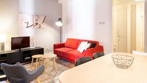 Ein modernes Wohnzimmer mit einem roten Sofa, einem Fernseher und einem Esstisch mit Stühlen.