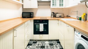 Una cocina con armarios blancos, microondas, tostadora, horno, lavabo y lavadora.