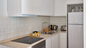 Eine moderne Küche mit weißen Schränken, einer schwarzen Induktionskochplatte, einer Edelstahl-Spüle und einem weißen Kühlschrank.