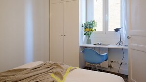 Ein Schlafzimmer mit Bett, Kleiderschrank, Schreibtisch mit Stuhl und einem Fenster mit Pflanze.