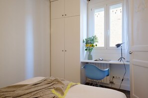 Un dormitorio con una cama, un armario, un escritorio con una silla y una ventana con una planta.