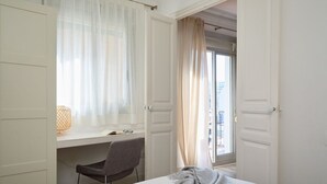 Hotellihuone, jossa on sänky, työpöytä tuolilla, ikkuna läpikuultavilla verhoilla ja näkymä ulos.