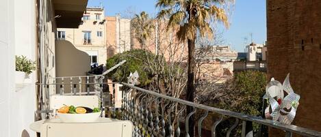 A balcony with a table and chairs, a decorative metal railing, and a palm tree in the background.