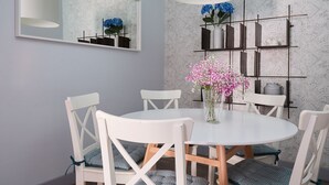 Ein Essbereich mit einem runden Tisch, weißen Stühlen, einer Vase mit Blumen, einem an der Wand montierten Regal und einem großen Spiegel.
