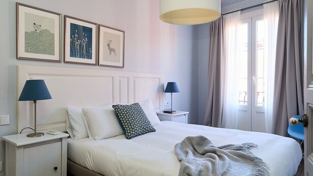 Ein ordentlich eingerichtetes Schlafzimmer mit einem Bett, zwei Nachttischen, einer Lampe und einem Fenster mit Vorhängen.