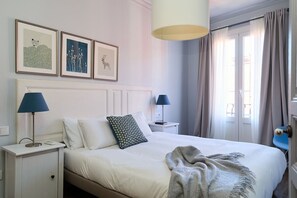 A neatly arranged bedroom with a bed, two bedside tables, a lamp, and a window with curtains. - Casa Cosi - El Farro 2 (Barcelona)
