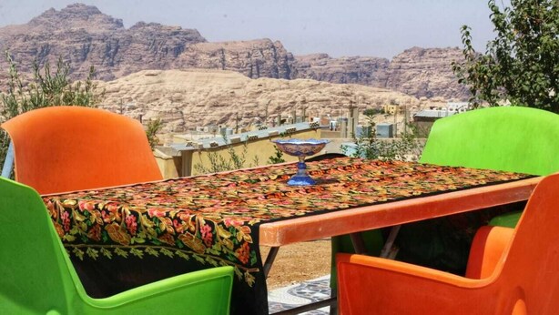 A table with a floral tablecloth, surrounded by colorful chairs, set against a mountainous backdrop. - Happy Family Apartment  (Wadi mousa)