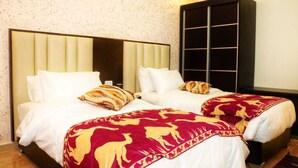 A hotel room with two beds, each with white bedding and a red and gold patterned throw blanket. There is a large black wardrobe with a mirrored door and a small table beside the beds. - Happy Family Apartment  (Wadi mousa)