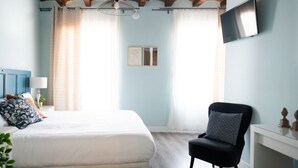 Une chambre à coucher avec un lit, une chaise, une télévision et une fenêtre avec des rideaux.
