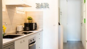 Une cuisine moderne avec des meubles blancs, une machine à café noire et une petite plante en pot.