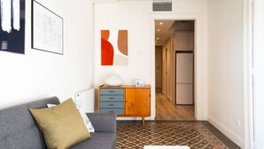 Una sala de estar moderna con un sofá gris, un tapete estampado, una mesa blanca y un mueble con cajones.
