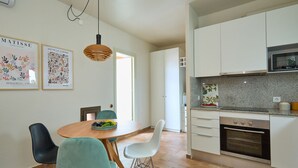 Una cocina moderna con armarios blancos, horno integrado y un comedor con mesa y sillas redondas.