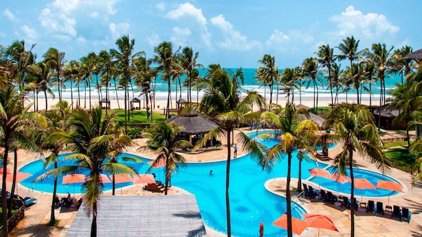 Un resort con un amplio espacio de piscina, palmeras y vista al mar.