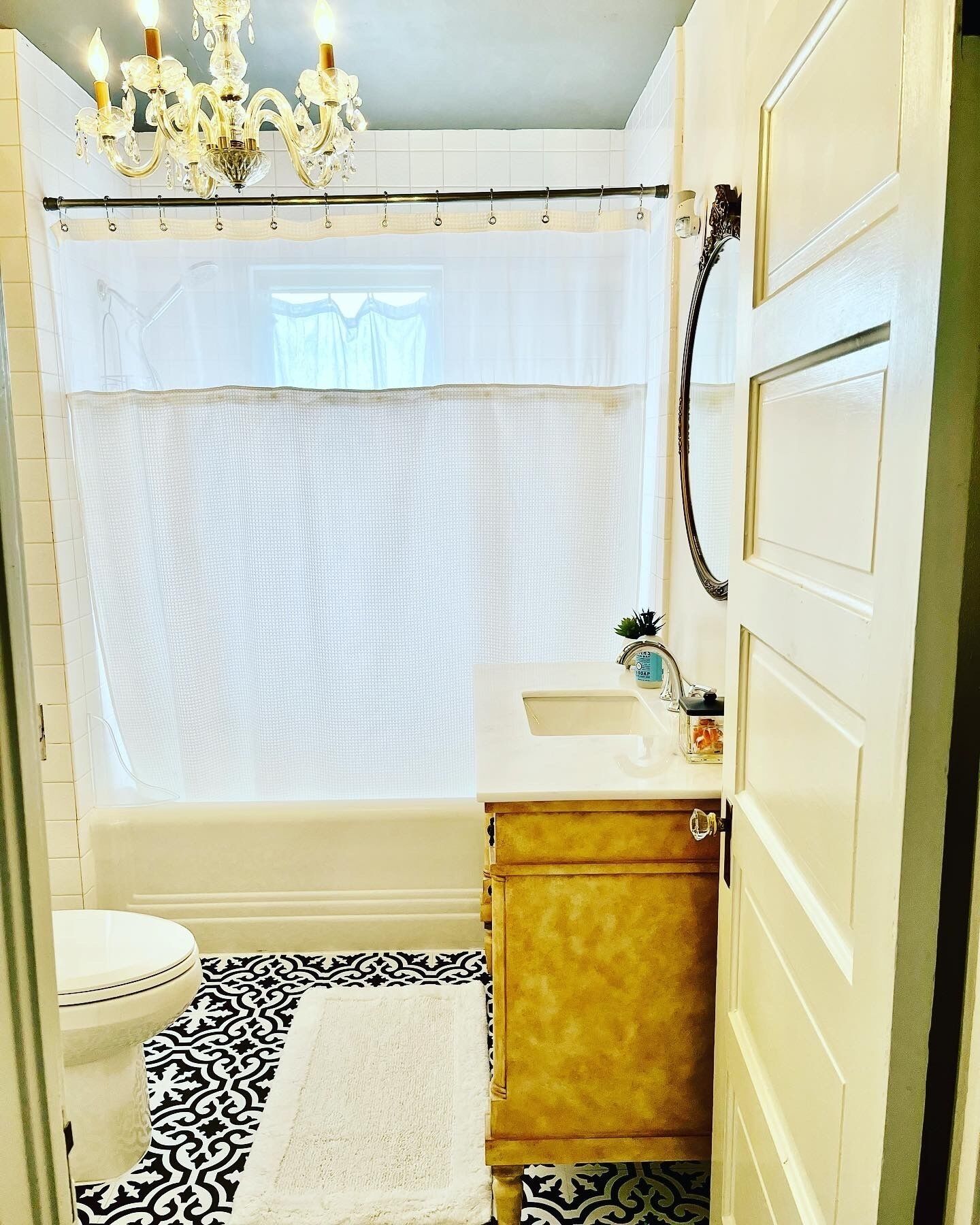 A bathroom with a bathtub, a white sink, a mirror, and a chandelier.