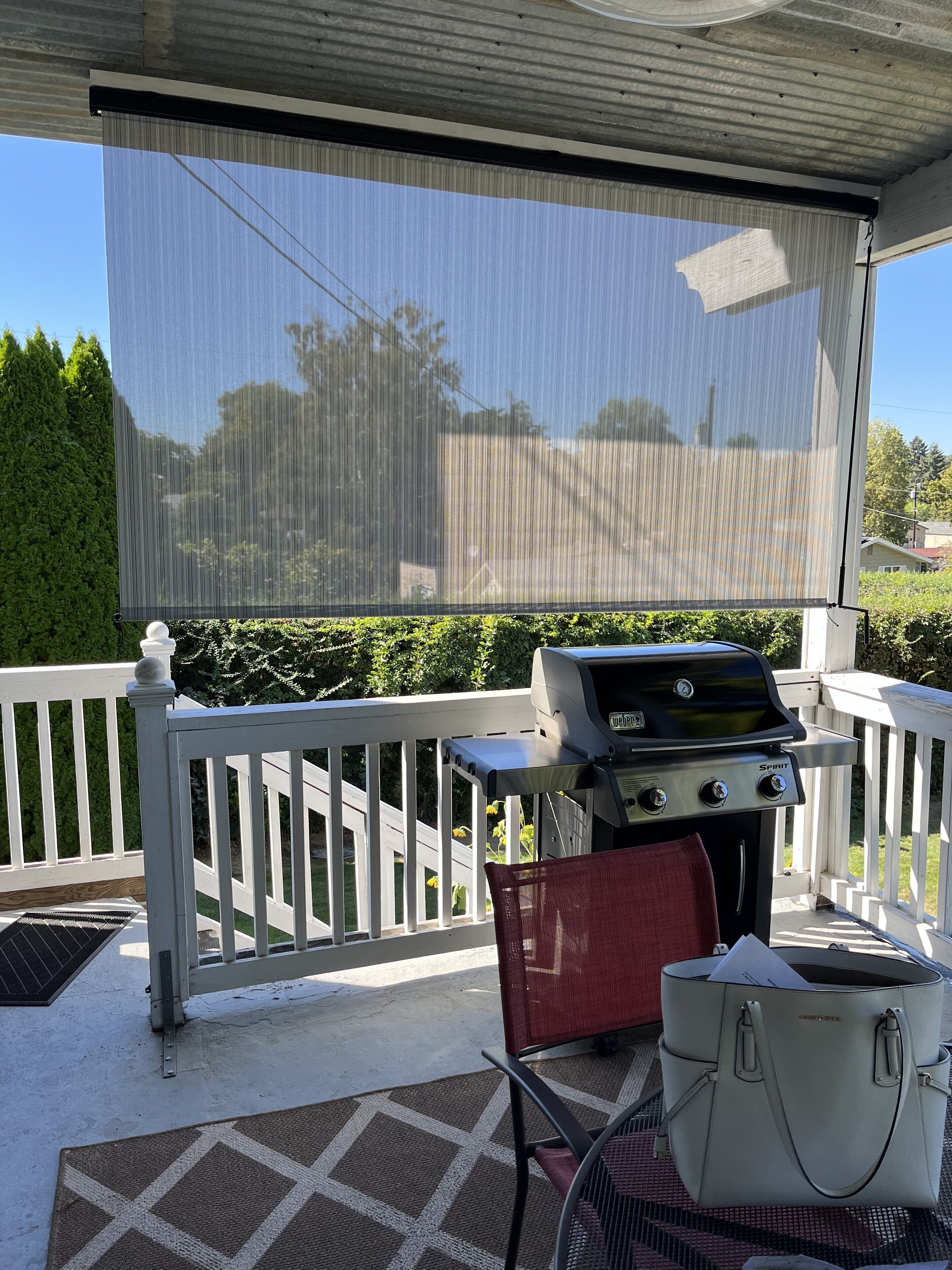 A covered outdoor area with a grill, a chair, and a bag on a doormat.