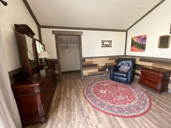 A room with a wooden floor, a red patterned rug, a black leather chair, a wooden dresser, a mirror, and a coat rack. - Loft apartment on a horse ranch (Austin)