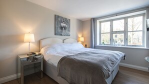 Ein Schlafzimmer mit einem großen Bett, zwei Nachttischlampen, einem Fenster mit Ausblick und einem Bild an der Wand.