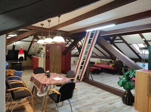 Um quarto de sótão acolhedor com uma mesa de jantar, cadeiras, um sofá e uma escada.