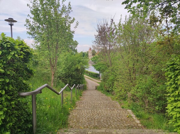 Stroll along the winding cobblestone path, lined with lush greenery and trees, towards a historic building with a tower.