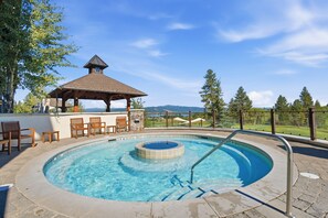 A swimming pool with a hot tub, surrounded by lounge chairs and a gazebo, overlooking a scenic landscape.