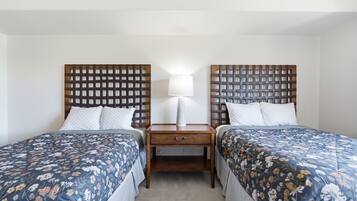 Habitación de hotel con dos camas individuales, una mesita de noche con lámpara y una pequeña mesa entre las camas.