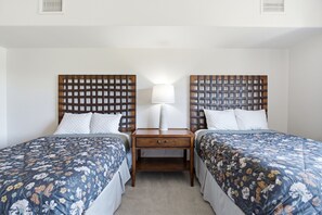 A hotel room with two single beds, a nightstand with a lamp, and a small table between the beds.