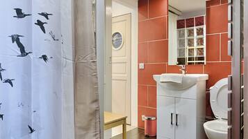 A bathroom with a white sink, red-tiled walls, a white toilet, and a small wooden stool.