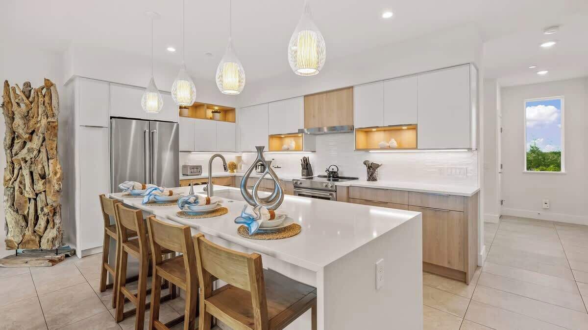 Una cocina moderna con una isla central, electrodomésticos de acero inoxidable e iluminación colgante.