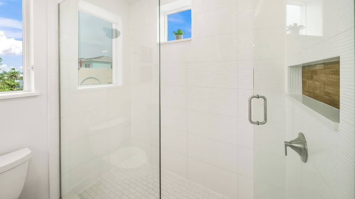 A modern bathroom with a glass shower enclosure, a window, and a wooden accent wall.