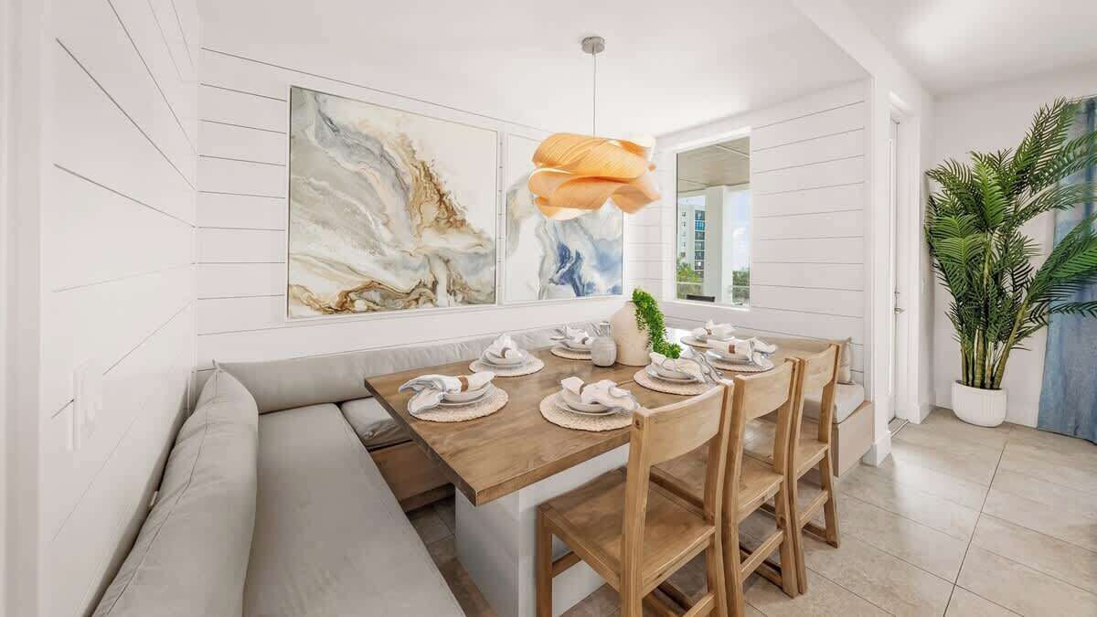 A dining area with a wooden table set for four, a bench, and a large abstract painting above.