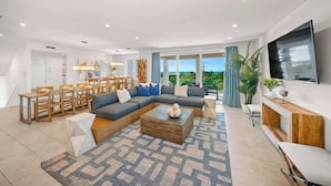 A modern living room with a sectional sofa, a coffee table, and a dining area with wooden furniture. - Steps to Beach/Gulf Views/Pool Volleyball/Slide (Siesta Key)