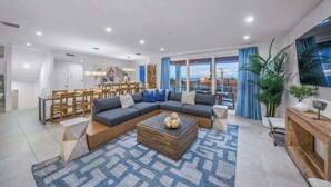 A modern living room with a sectional sofa, a coffee table, and a dining area with wooden furniture. - Steps to Beach/Gulf Views/Pool Volleyball/Slide (Siesta Key)