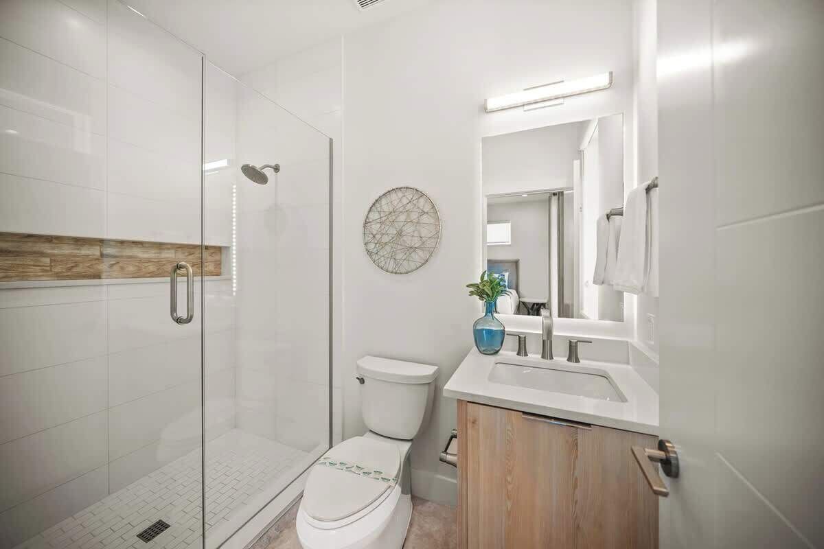A modern bathroom with a glass shower enclosure, a toilet, and a vanity with a mirror.